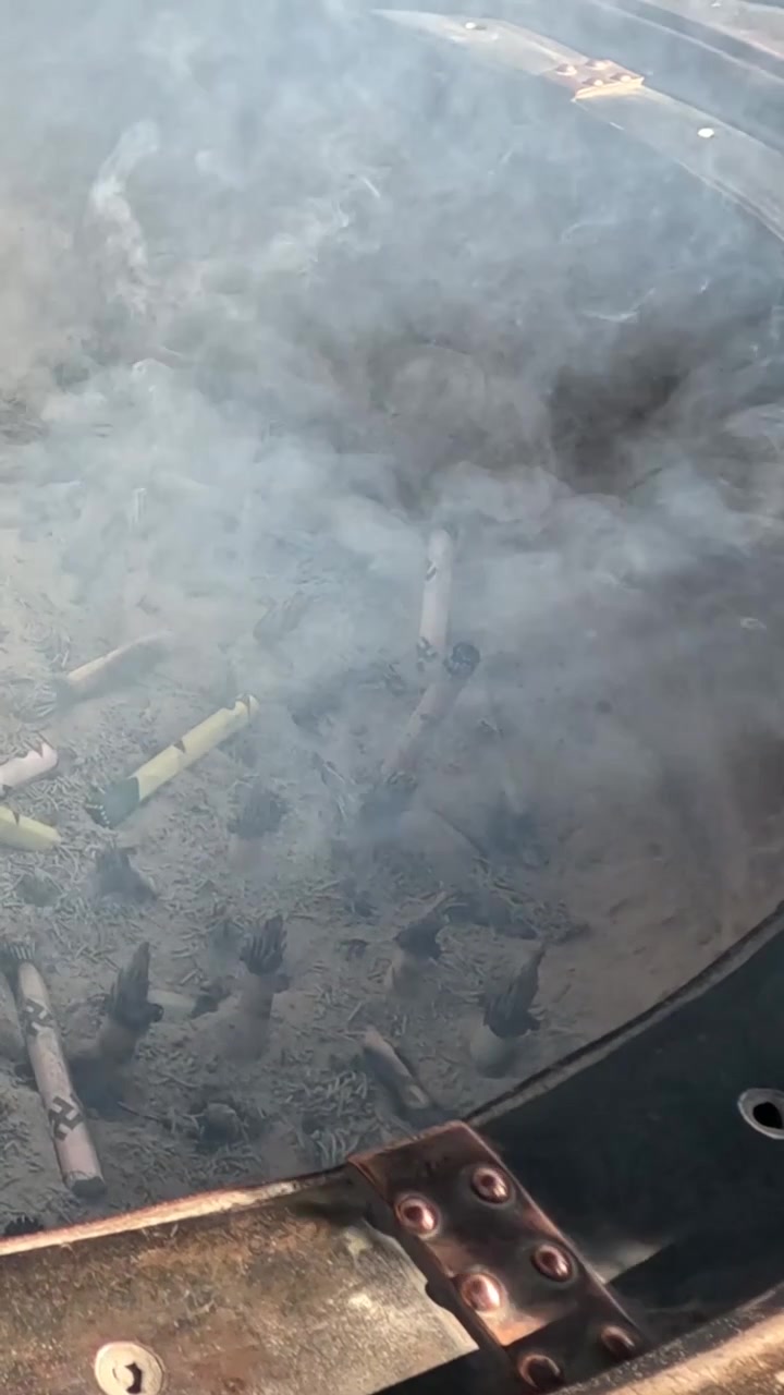 A person places burning incense sticks into a large metal container filled with white smoke.