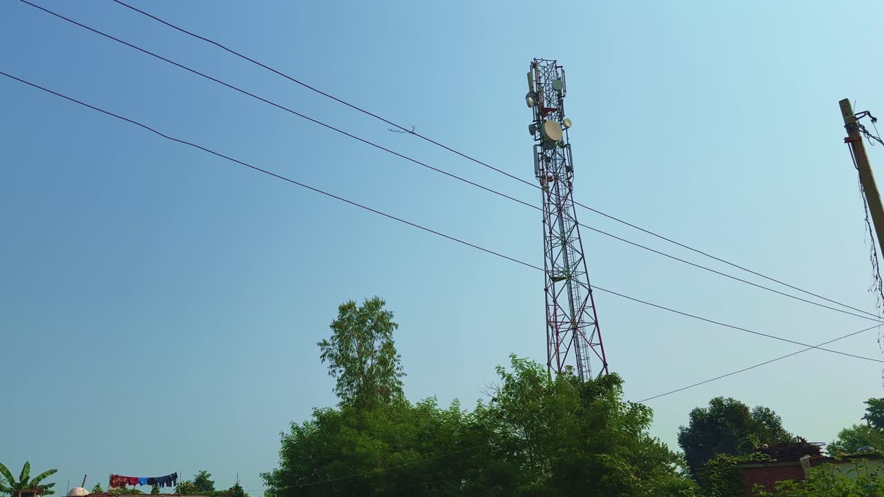 Smooth tilt-up shot from a rural brick house and farmland to a tall telecom tower with power lines under a bright blue sky, symbolizing connectivity in the countryside