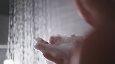 woman with foam on palms in shower unit closeup. relaxed lady blows soft soap froth enjoying warm bathe in wash room. funny hygienic procedures