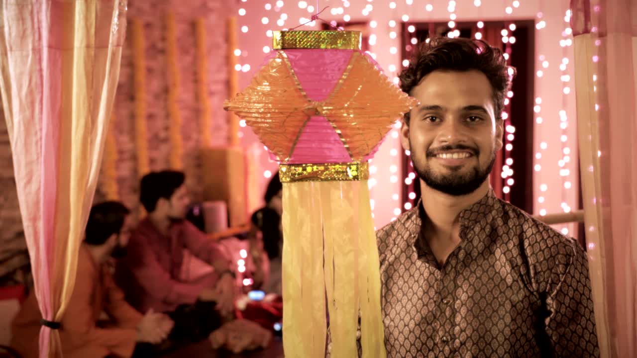 Un giovane uomo che indossa una kurta e appende colorate Diwali Kandil, mentre i suoi colleghi sono seduti e parlano sullo sfondo