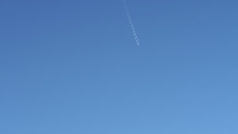 plane in the distance in an open cloudless sky leaving a trail of white smoke