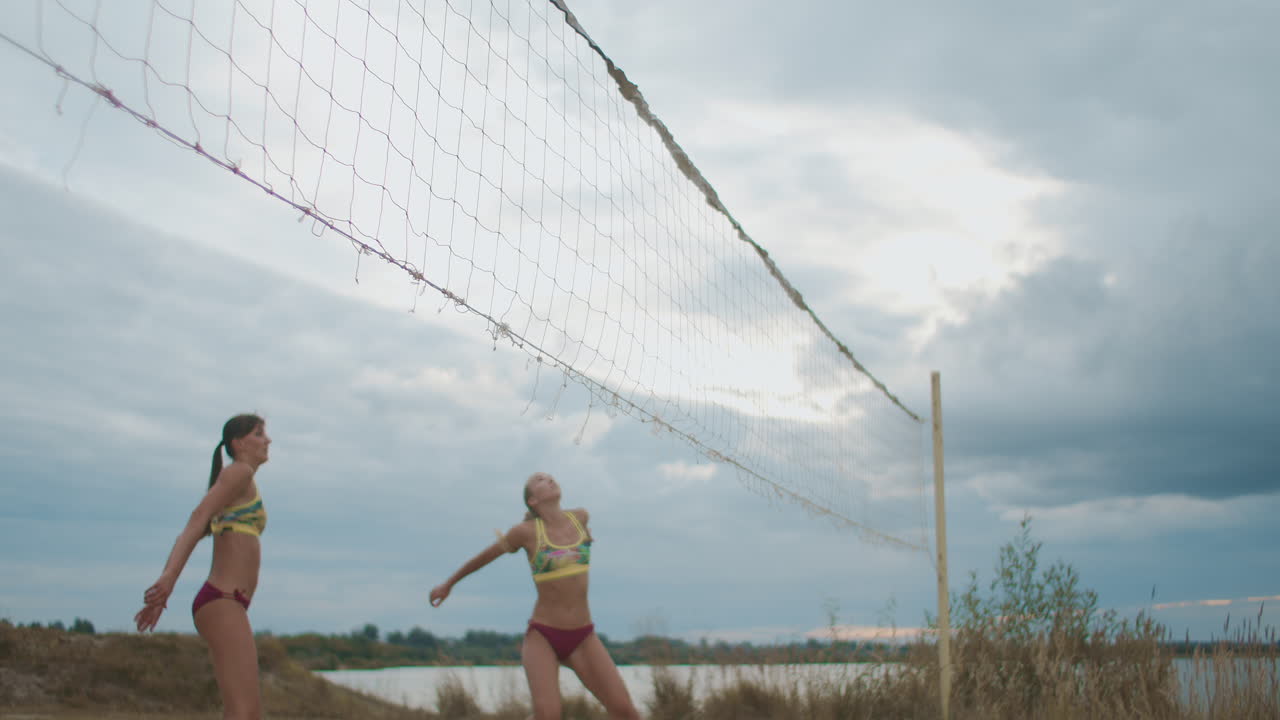 두 명의 프로 배구 선수 여성이 열린 해변 코트에서 다른 팀을 공격하고 있습니다.