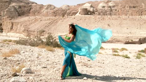 beautiful female dancer. belly dance. desert. sexy green blue dress dancing. long shot.