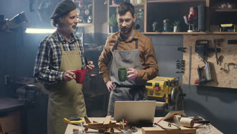 due falegnami in piedi in officina e guardano un video sul tablet mentre bevono caffè nel laboratorio di falegnameria