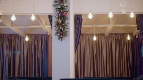 decorative winter holiday scene with glowing light bulbs hanging above soft purple curtains. christmas garland with pinecones, baubles, and snowflakes create a festive atmosphere in modern interior