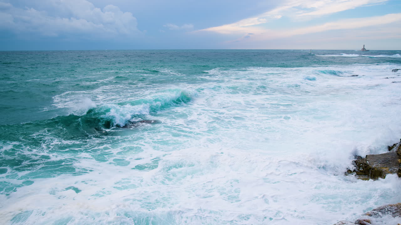 큰 바다 파도가 바위가 많은 해안에 부서져 거품과 안개, 불안한 바다에 등대 구멍과 추기경 표시를 만듭니다.