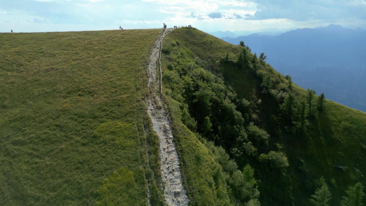 Vista aerea di escursionisti che camminano lungo un sentiero erboso in cresta con un paesaggio montano in lontananza.