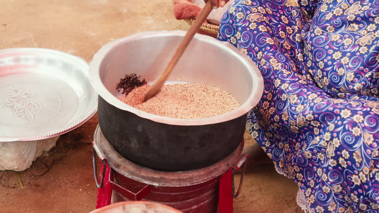 una mujer negra está agitando una gran olla de sésamo con una cuchara de madera.