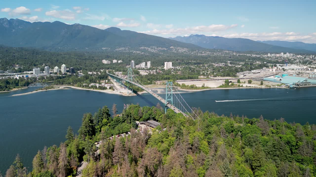 Filmato aereo con drone del Lions Gate Bridge vicino a Stanley Park a Vancouver, che mostra il ponte sospeso che attraversa le acque costiere con una penisola boscosa e lo skyline della città sullo sfondo.