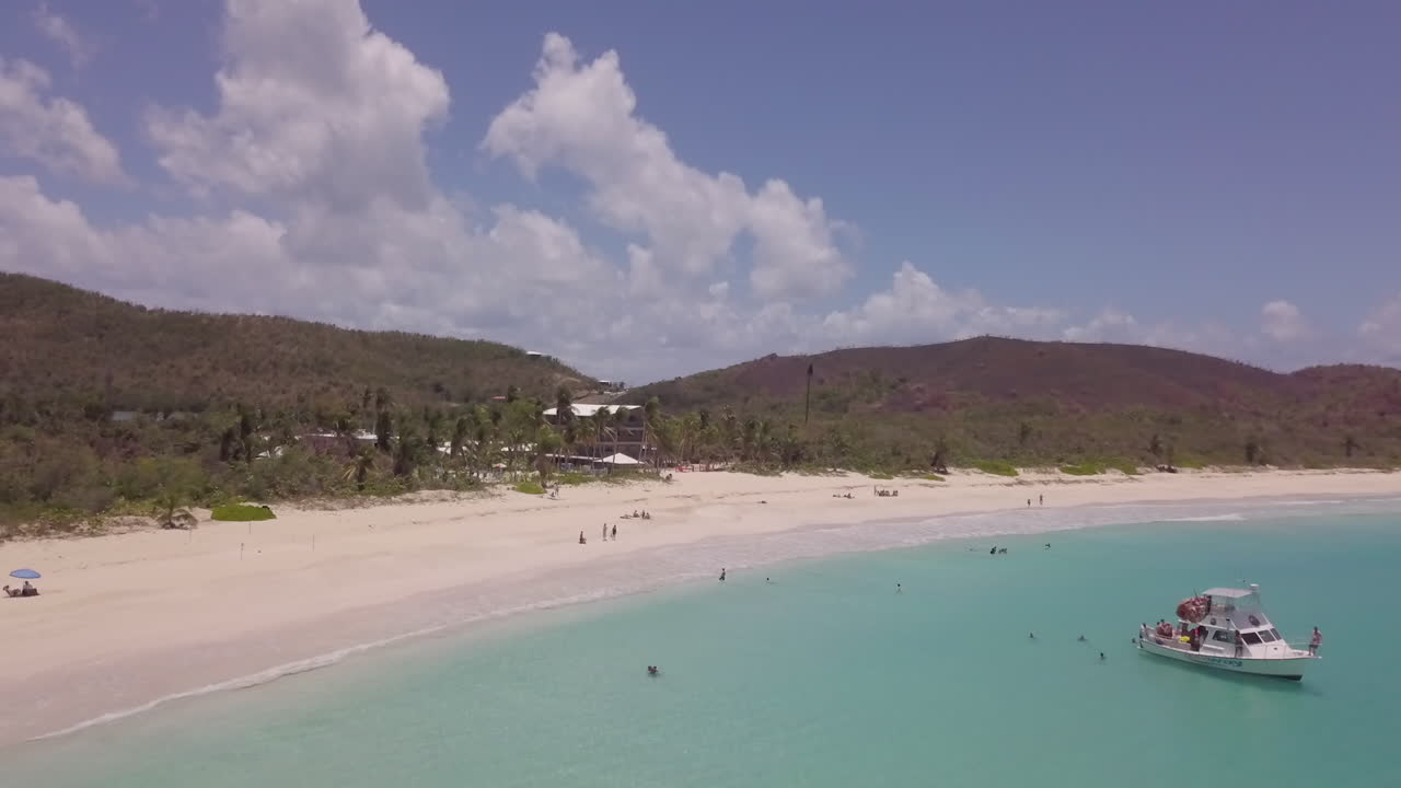 Aerial footage of a boat moored at Flamenco Beach in Puerto Rico, people are swimming in the water and lying on the beach.