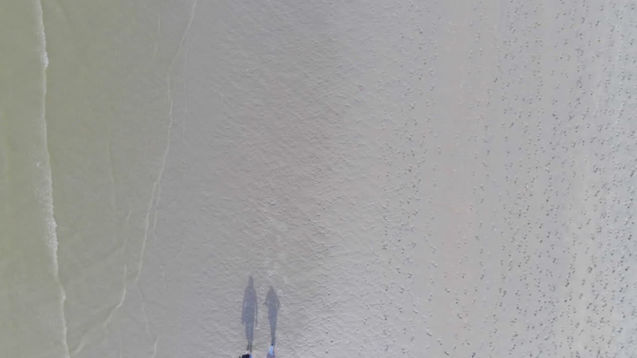 해변 옆의 모래사장을 걷는 사람들의 실루엣을 위에서 아래로 오름차순