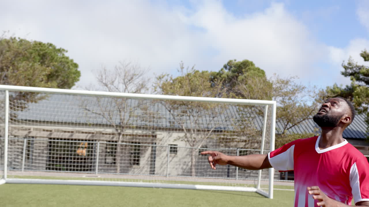 Playing soccer, african american man in red jersey looking up near goalpost on field
