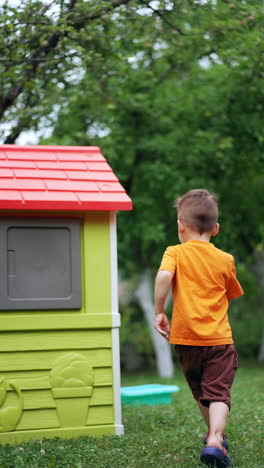 little caucasian baby boy walks outdoors. kid turns to the playhouse and slams the doors. vertical video.