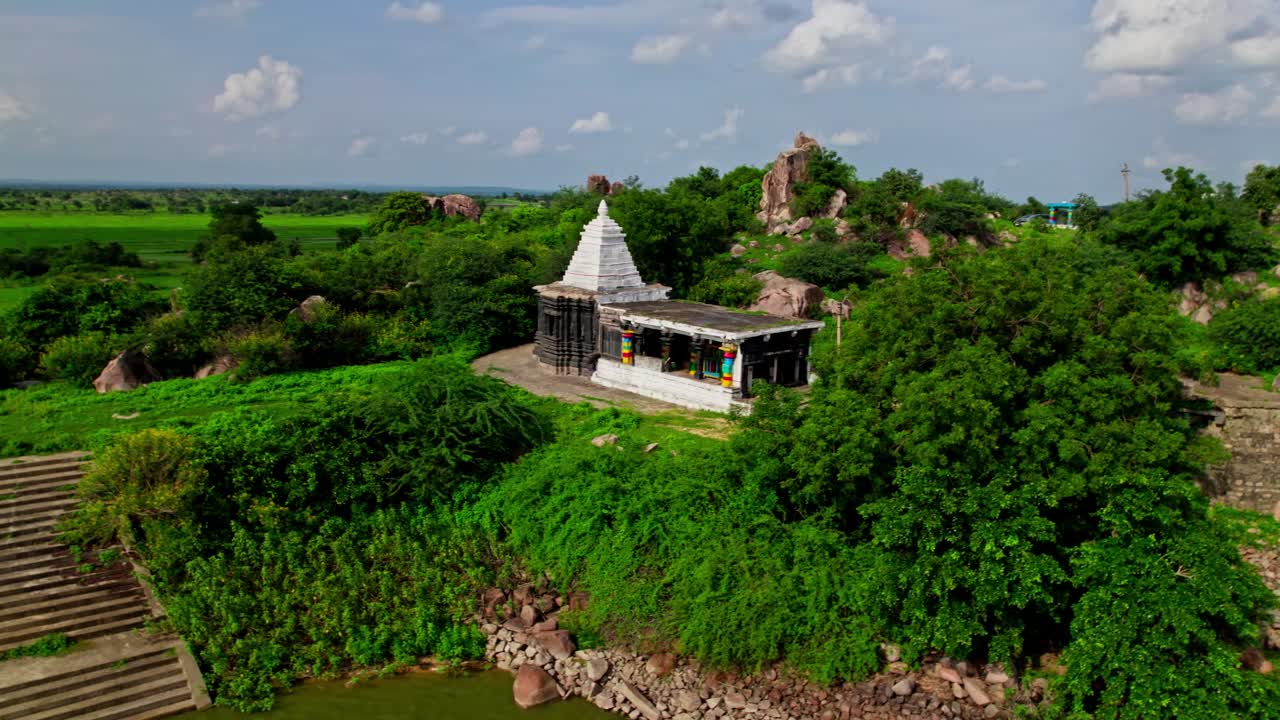 old construction temple with signal tower in the background agricultural land at yelupu gonda, surampally, tekmal, telangana, india. day time, semi circle shot, drone shot, 4k.