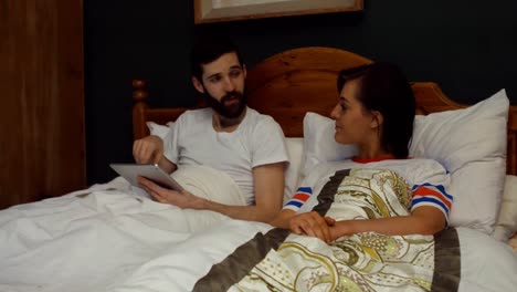 Couple-using-digital-tablet-on-bed-in-bedroom