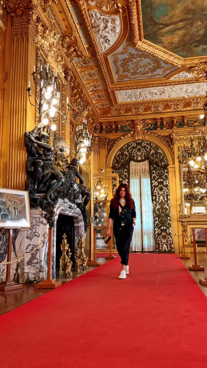 Boston, USA, 5 maggio 2025: Donna che cammina verso la telecamera all'interno di una grande sala da ballo dorata. Inquadratura a figura intera di una donna in abiti neri che cammina su un tappeto rosso in una sala dorata riccamente decorata.