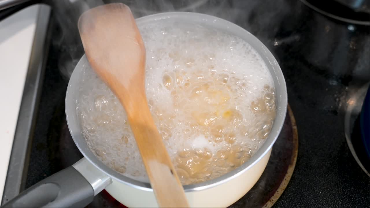 Den enkle komforten av et hjemmelaget måltid er fanget i dette bildet av pasta som koker i en kasserolle. En treskje på kjelen bidrar til den autentiske, rustikke følelsen.