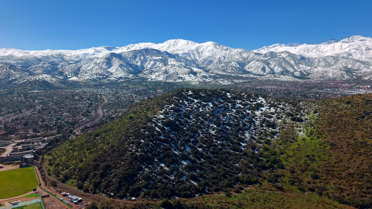 Flying over Medio Hill and the snow-capped Andes Mountains in the Lo Barnechea district of Santiago on a sunny day, Chile