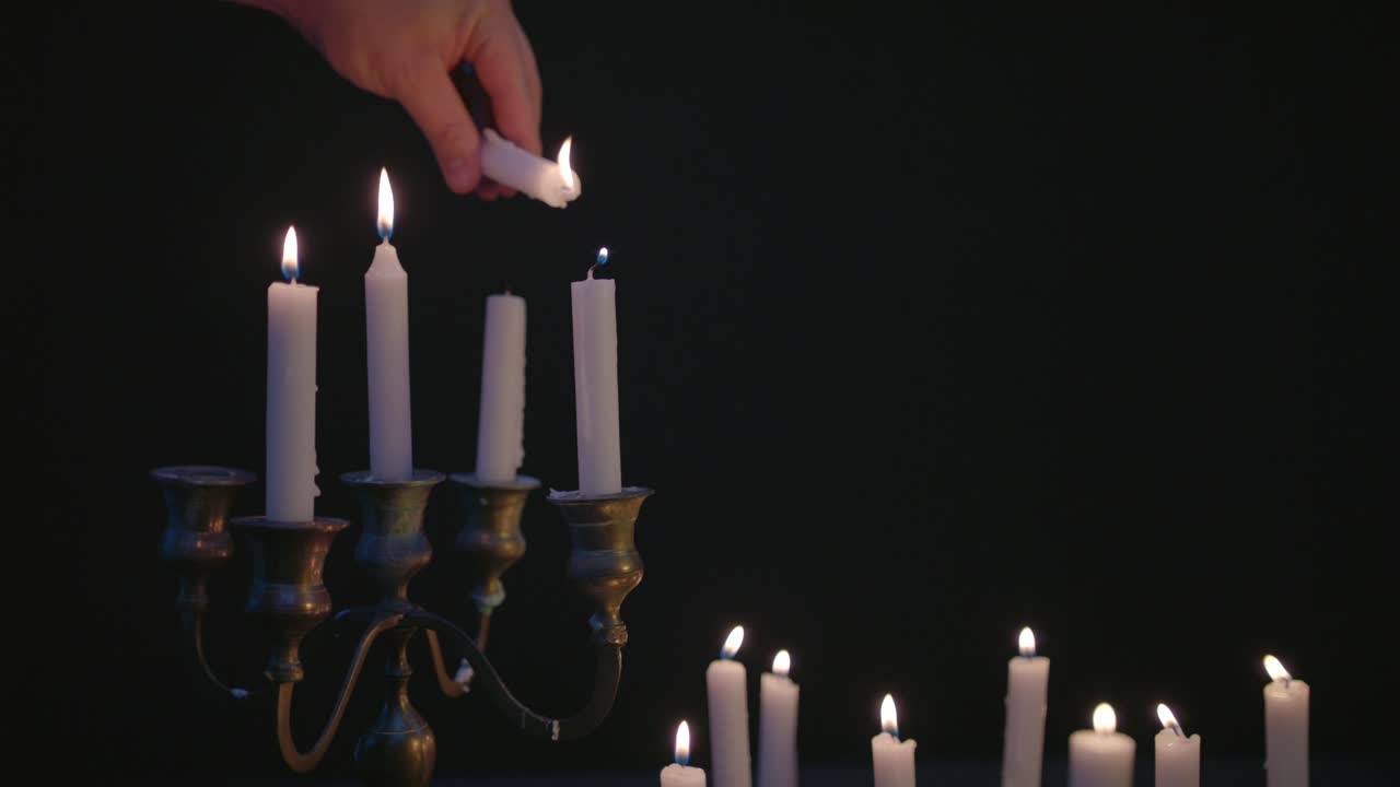 una vela blanca enciende unas pocas velas en un candelabro con un grupo de velas blancas encendidas y funcionando durante un rato a cámara lenta