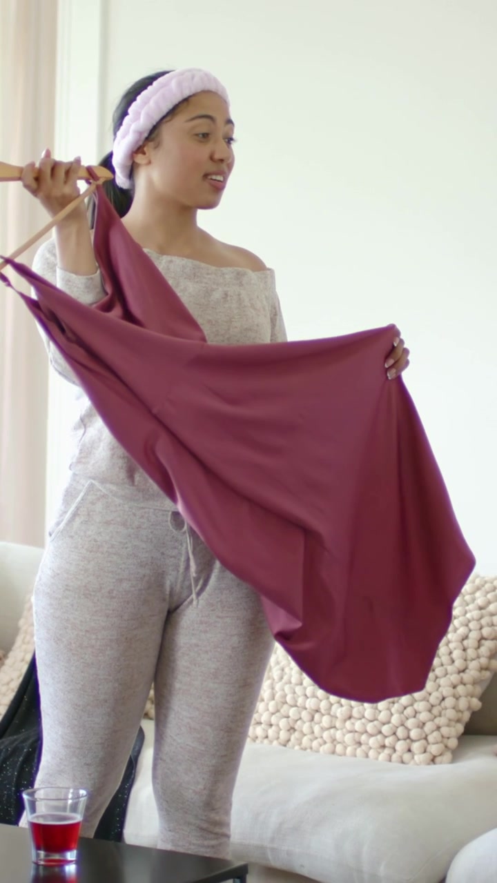 Video verticale: Prendendo una gruccia, donne in abbigliamento da casa scelgono abiti verdi e magenta vicino al divano.