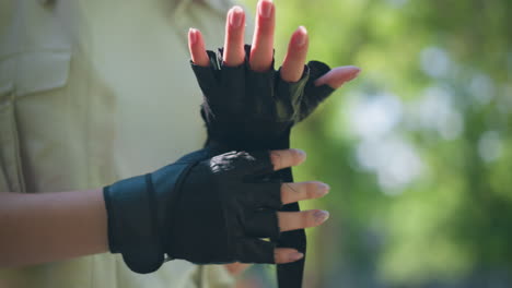 close-up of individual outdoors fastening biker glove on left hand with focused gesture, background shows blurred trees and lush greenery