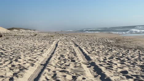 sandy beach with a trail of tire marks on the sand and beach-breaking waves