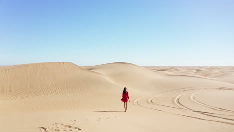 drone following a woman in a red dress walking barefoot in the desert