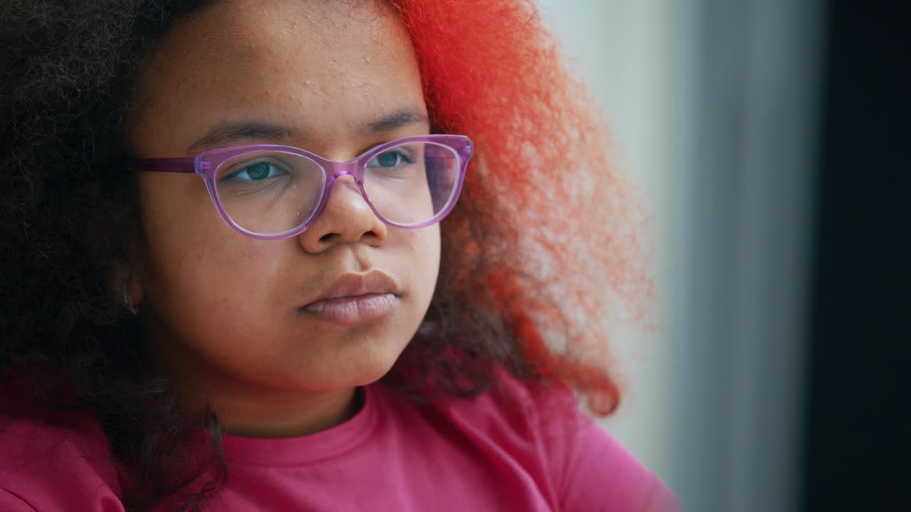 Focused young student with partially red hair and glasses looking downwards while deeply engaged in learning, embodying concentration and intellectual curiosity
