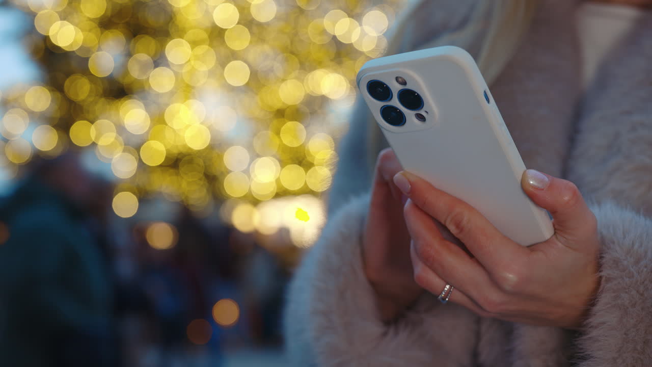 Woman using smartphone with Christmas lights in background