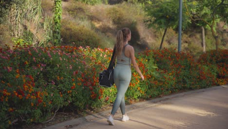 la chica con cola de caballo, vestida con ropa deportiva y llevando una bolsa, camina por la calle con la espalda volteada