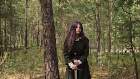 girl in vintage garment sticks sword into ground in forest