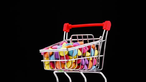 primer plano de un carrito de supermercado lleno de coloridos dulces de chocolate girando en la mesa giratoria. aislado en el fondo negro.