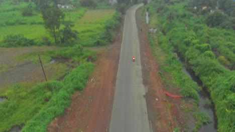 Pan-tilt-down-drone-shot-of-red-scooter-motorcycle-rural-Indian-road