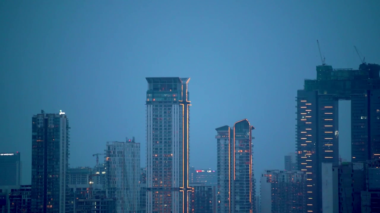 Toma panorámica aérea con zoom de dron mostrando rascacielos urbanos y edificios en construcción de noche en Bombay, Hyderabad, Bangalore a la hora azul con grúas de construcción y luces.