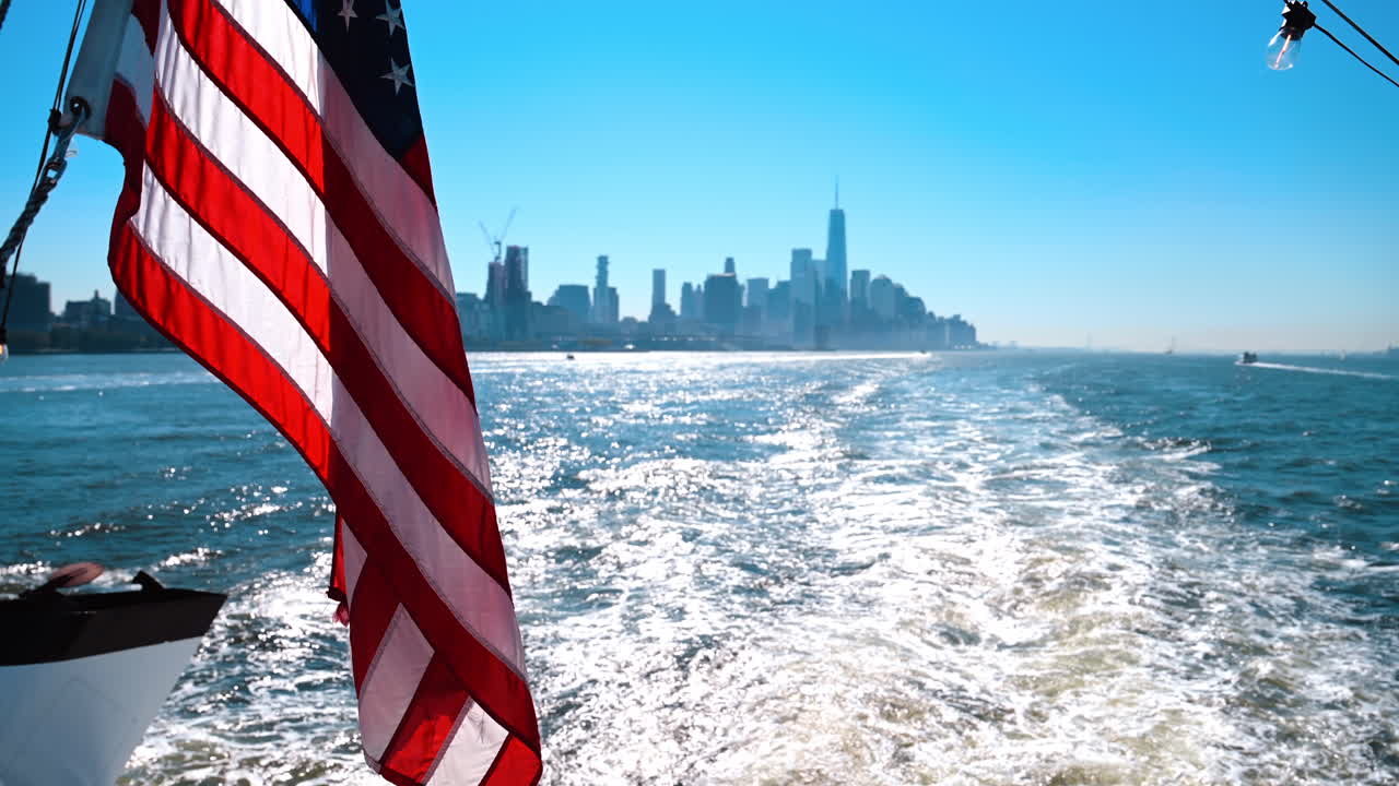 Bandiera americana su un traghetto con vista su Manhattan. Bandiera americana che sventola dal retro di un traghetto con lo skyline di Manhattan illuminato dalla luce del sole