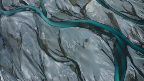 top down drone shot of blue glacial braided river veins and streams weave and flow through grey landscape, new zealand