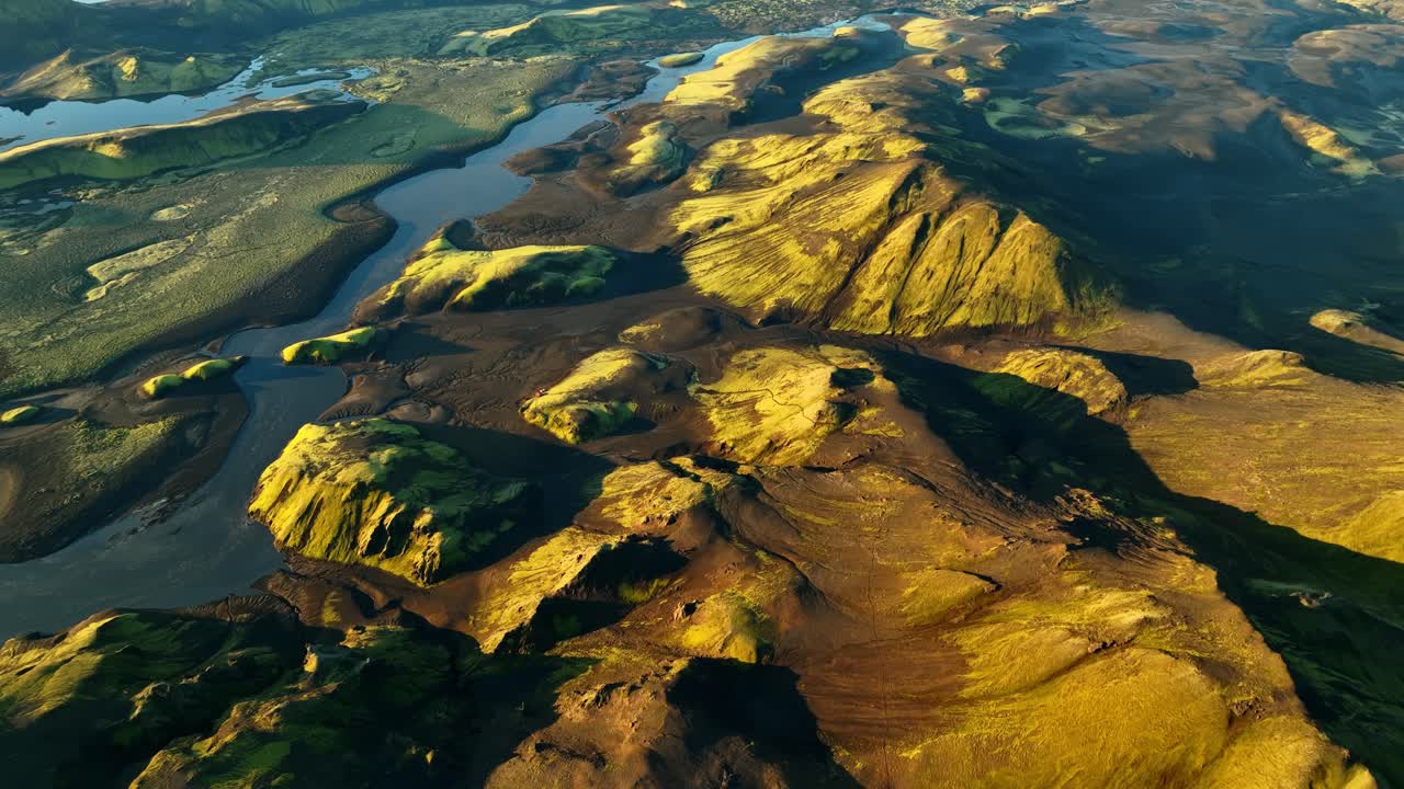 Vuelo rápido con dron sobre las colinas volcánicas de las tierras altas de Islandia y el río serpenteante; el sol de la hora dorada ilumina las crestas cubiertas de musgo y los oscuros valles de lava para obtener vídeos de paisajes de aventura épicos