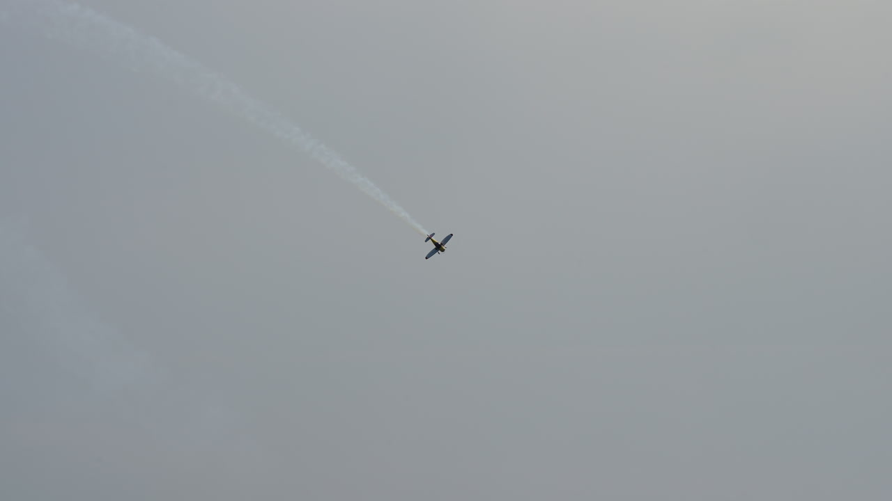 Aerobatic aircraft flies straight up into the sky leaving white smoke trail behind
