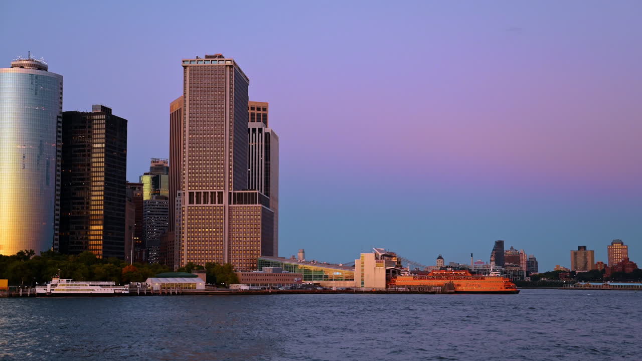 New York, Hoa Kỳ, ngày 2 tháng 8 năm 2025: Phà màu cam tại bến Manhattan trong hoàng hôn tím. Quang cảnh bến phà và con tàu màu cam với bầu trời hồng và tím trên Thành phố New York.