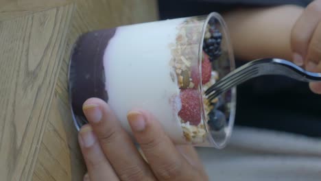 person eating a healthy acai bowl or yogurt parfait with berries and granola