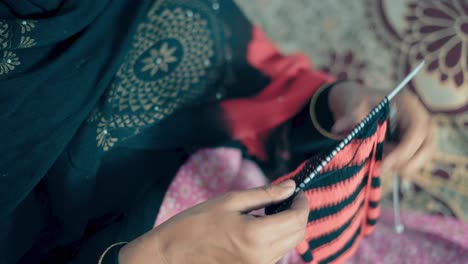 footage from above of woman's hands knitting with needle crafts and red and black wool