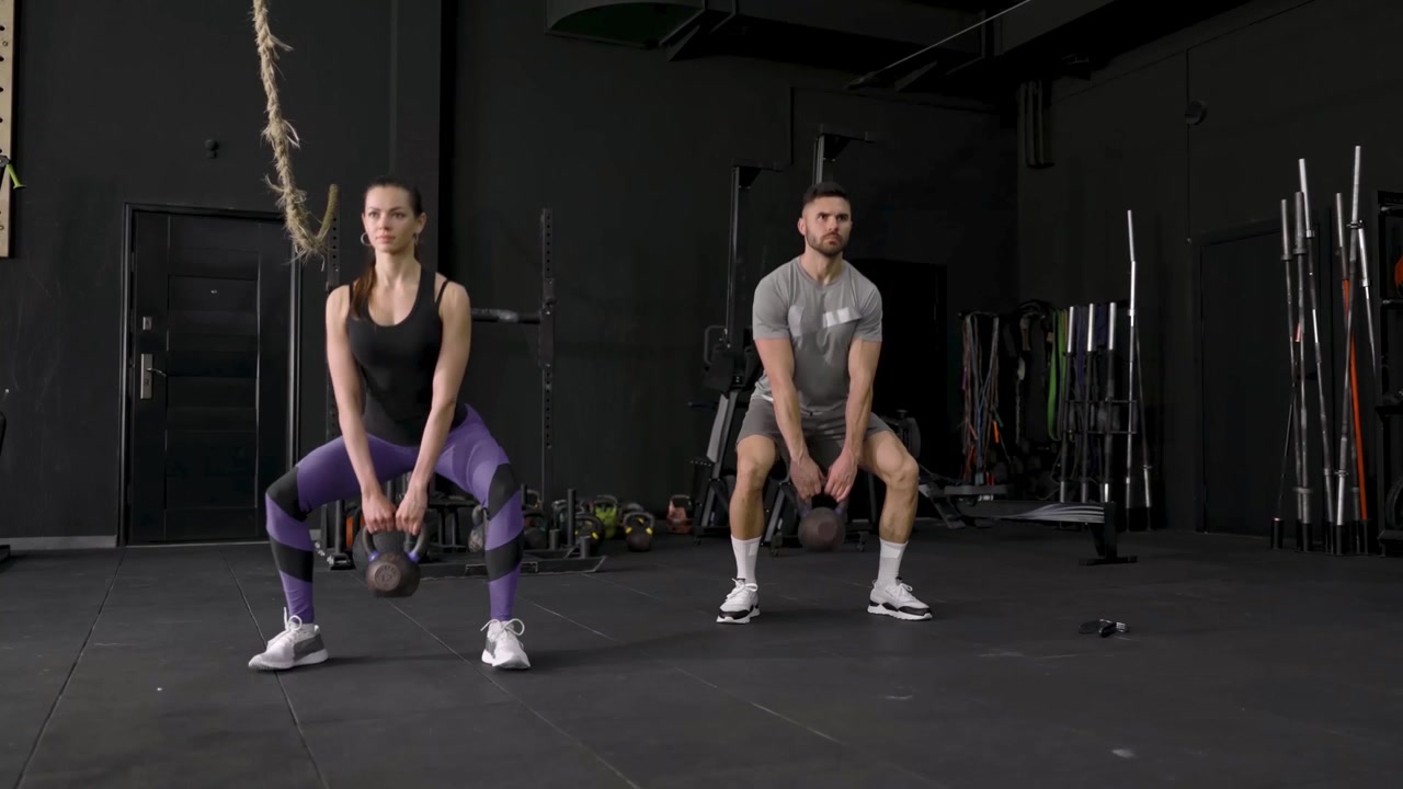 Uomo e donna che eseguono squat con kettlebell in palestra