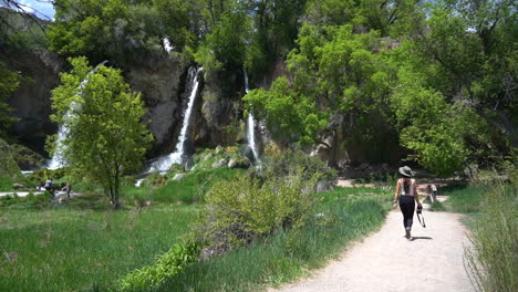 back of young female photographer walking with camera on path under waterfalls