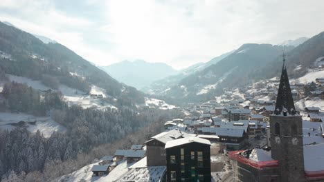 drone flying backwards over a small swiss mountain town in winter and revealing a church in the village center