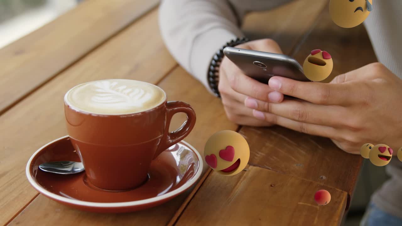 Man tapping phone on cafe table, causing reaction emojis swirling around red cup for marketing