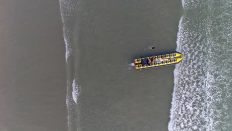 Zenith-Luftdrohne-Mit-Blick-Auf-Ein-Bananenboot,-Das-Ins-Wasser-Kommt-Und-Von-Menschen-Geschoben-Wird