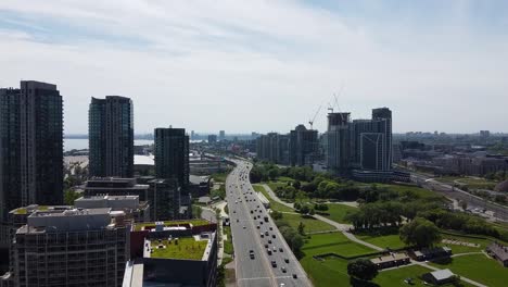 aerial shot flying over a toronto highway next to a park in the summer