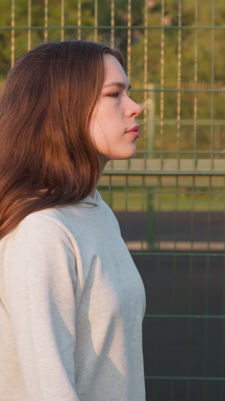 한 여성이 시내 경기장의 울타리를 걸어가며, 젊은 여성은 신체 건강을 향상시키기 위해 피트니스 수업에 갔고, 해가 지면 문제에 대해 생각하고, 외로움의 느낌을 느다.