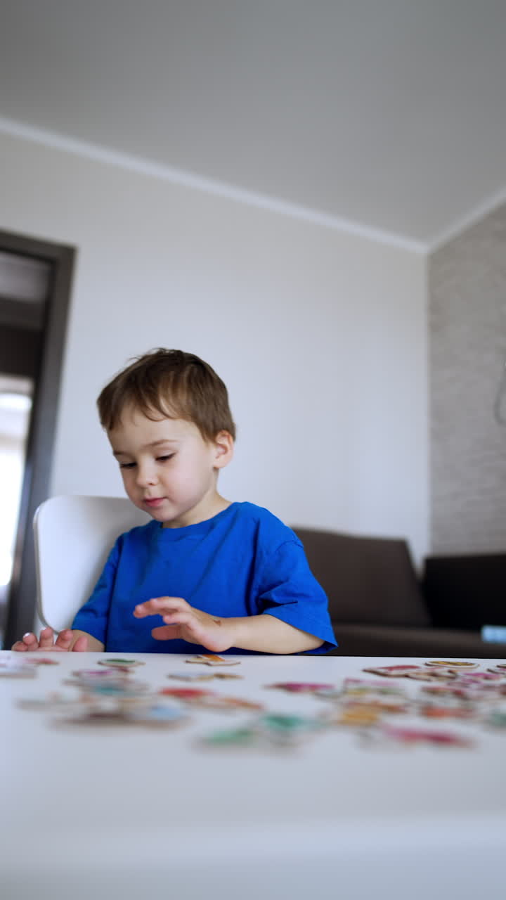 Kid looks at the puzzles scattered on the desk in front of him. Toddler boy stands up and runs away. Vertical video.