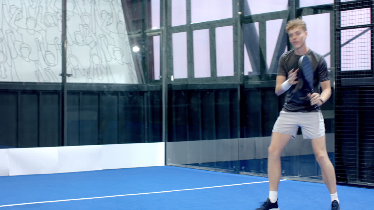 Young man playing padel tennis, swinging racket on indoor court